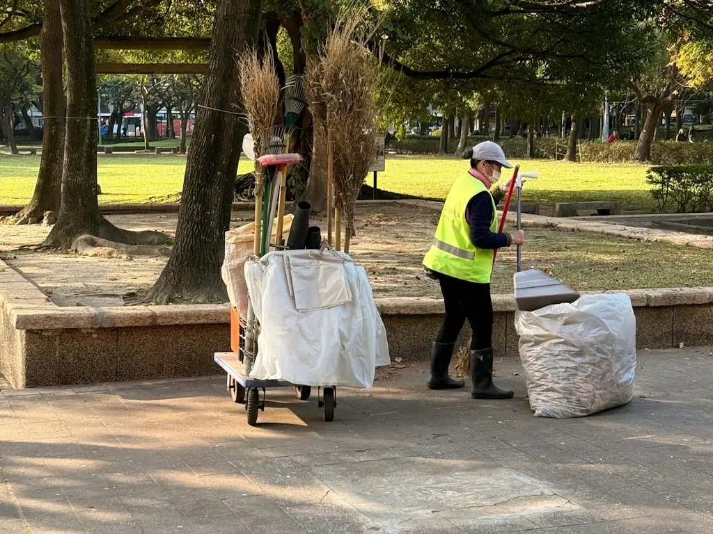 A porter in a safety vest with a cart, picking up litter